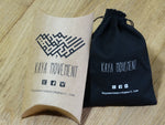 Two packaging items from "Kaya Movement" are showcased: a brown cardboard pillow box and a black drawstring pouch, both adorned with the brand logo and contact email, kayamovement@gmail.com. These stylish packages also display social media icons for Facebook, Twitter, and Instagram—perfect for your Unique Gold Triangle Septum Ring with Onyx, Piercing 8mm - 18g.