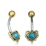 A pair of DORE Butterfly Belly Bars in gold by Kaya Movement, featuring elaborately designed heart-shaped ends with a central natural turquoise stone surrounded by intricate gold details. These curved rings have a 14 gauge surgical steel silver-colored shaft.
