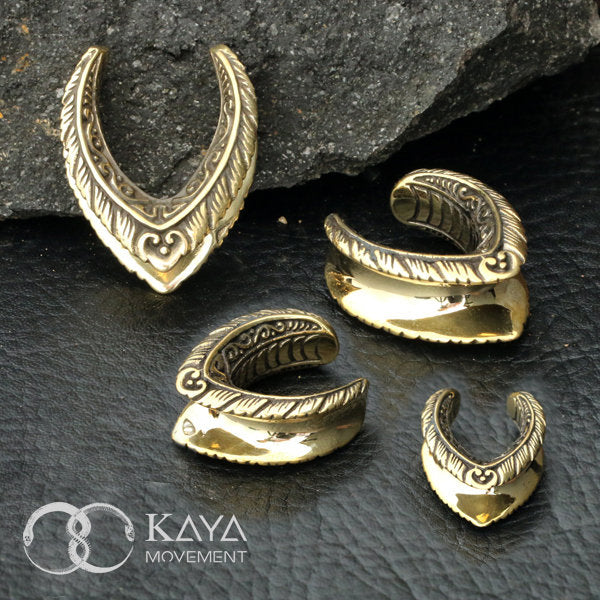 A display of four intricately designed MYRI Tribal Saddle Tunnels in gold, ranging from 12mm to 25mm gauge, is set against a dark, stone background. The tunnels feature detailed ethnic patterns and leaf-like motifs. The "Kaya Movement" logo and name are visible in the bottom left corner.