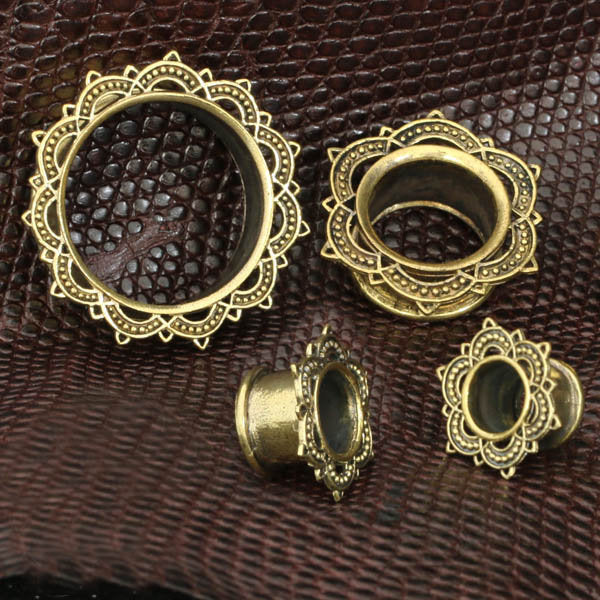 A close-up image of four LOTUS Sacred Lotus Mandala Round Tunnels in silver, created by Kaya Movement, arranged on a textured dark brown surface. The handcrafted tribal plugs vary in size from 4mm to 25mm gauge and are designed for stretched ear piercings.