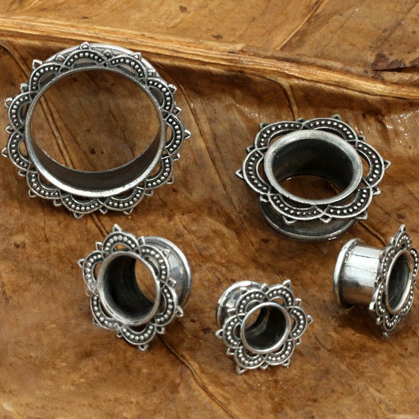 A set of Kaya Movement's LOTUS Sacred Lotus Mandala Round Tunnels in Silver, available in sizes from 4mm to 25mm gauge, each featuring an intricate Lotus flower pattern around the edges, displayed on a textured brown surface.