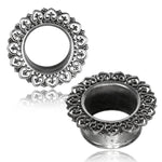 Two ornate silver ear plugs from Kaya Movement's ONAS Sacred Lotus Mandala Round Tunnels, featuring intricate lace-like designs around the edges. The decorations include heart-shaped patterns, giving the plugs a delicate and vintage appearance. One tribal plug is placed flat, showcasing its full design, while the other stands upright. Available in gauges from 3mm to 18mm.