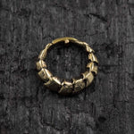 The AARO Cyborg Seamless Hoop Septum Nose Ring in Gold by Kaya Movement, featuring an 18 gauge design and an irregular, segmented appearance, rests on a textured, dark gray surface. The rough, uneven segments give the ring a rugged, ancient appearance.