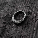 A close-up shot of Kaya Movement's AARO Cyborg Clicker Hoop Septum Nose Ring in silver, placed on a dark, weathered wooden surface. The 925 silver ring showcases a design with a sequence of irregular, rough-hewn segments, blending the aesthetic of dystopian body jewelry with a rugged and unique appearance.