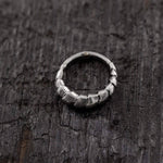 Close-up of the Kaya Movement AARO Cyborg Clicker Hoop Septum Nose Ring in Silver, featuring a unique, textured, and slightly irregular design placed on a dark, weathered wooden surface. The ring has a chunky and rugged appearance, suggesting it may be handmade or crafted with a distinctive artistic style.