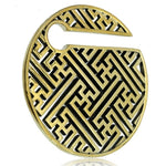 The SAYL Sayagata Disc Ear Weights in Gold by Kaya Movement feature a round, golden metal pendant with an intricate geometric cutout pattern of interlocking lines. Similar to other Massif Sayagata ear weights, the top has a notch creating a small gap in the circle. The polished brass hoop offers a shiny appearance against the white background. These are designed for 00 gauge sizes.