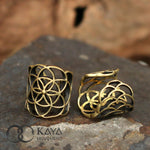 Two intricately designed gold accessories displayed on a stone surface. One piece is the Flower of Life Ear Cuff in Gold featuring a geometric flower pattern, while the other showcases an overlapping scale-like design. The Kaya Movement logo is visible in the lower left corner.