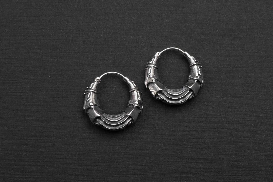 A pair of Kaya Movement's Bio Organic Silver Hoop Earrings with intricate details on a black background. These earrings feature a layered design with ornate patterns, giving them a unique and stylish look reminiscent of cyberpunk style jewelry.