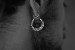 Close-up black and white image of a person's ear adorned with Kaya Movement's Silver Futuristic Hoop Earring. The sterling silver earring showcases intricate, decorative patterns with a hint of cyberpunk design. The person's face is partially visible, highlighting the detailed craftsmanship of this unique tech lover gift.