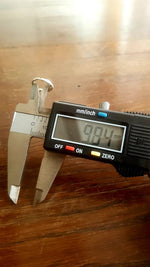 The AYM Seamless Septum Ring in Silver (18 gauge) by Kaya Movement is being measured with a digital caliper. The screen on the caliper displays a diameter of 9.84 mm for this piece of 925 sterling silver jewelry. The black-bodied caliper, with buttons labeled "OFF," "ON," and "ZERO," is positioned on a wooden surface to take the measurement.