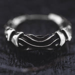 A close-up of the Silver Futuristic Hoop Earrings by Kaya Movement placed on a dark textured surface. The earrings feature a rugged, interwoven design with smooth and ridged sections, giving them an intricate, handcrafted appearance reminiscent of cyberpunk design. The dark background contrasts sharply with the shiny metal of the earrings.