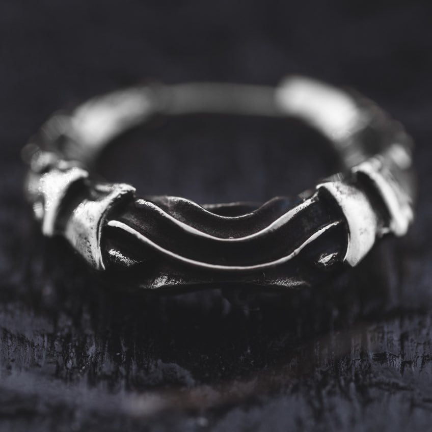 A close-up image featuring the Bio Organic - Silver Hoop Earrings by Kaya Movement, showcasing their rugged and irregular design on a textured black surface. Reminiscent of cyberpunk style jewelry, these earrings feature a series of overlapping metal bands that give them an intricate and unique appearance, embodying futuristic alien xenomorph aesthetics inspired by H.R. Giger.