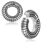 A close-up of two SILO Seamless Hoop Ear Weights in Silver with Clicker by Kaya Movement, designed with a pattern of raised dots along the surface. The ear weights, resembling minimalist silver earrings, have a rustic, antique finish. One is shown fully closed while the other is partially open, displaying the clasp mechanism.
