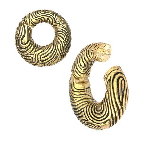 Introducing the UMI Hoop Ear Weights in Gold with Clicker by Kaya Movement. These 2-gauge brass hoops combine an intricate, abstract line pattern with a unique design: one earring is fully closed in a circular shape, while the other features a slightly opened form for a modern, edgy look. The oxidized brass finish and organic grooves add texture and detail to these statement pieces.