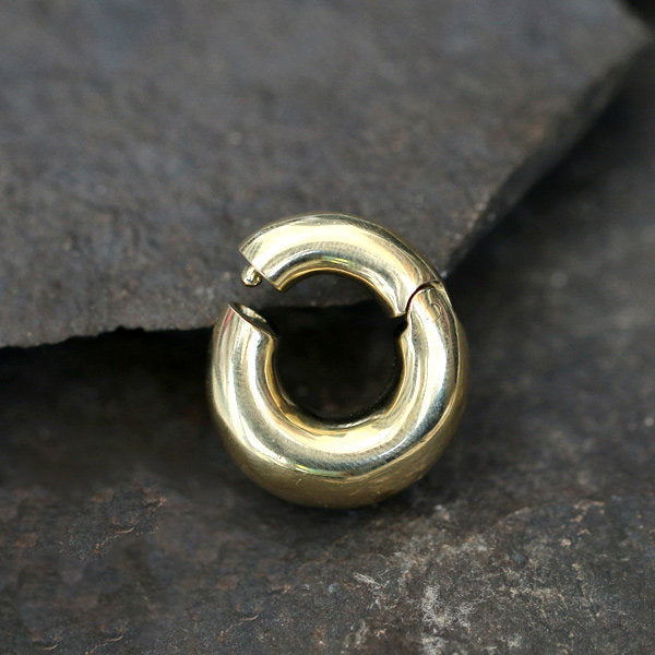 A close-up image of the DAYA Minimalist Hoop Ear Weights in Gold with a clicker by Kaya Movement, featuring a smooth and polished finish. The 2 gauge earring rests on a textured, dark gray stone surface—perfect for those seeking stylish unisex body jewelry.