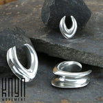 Three silver MYRA Minimalist Saddle Tunnels are displayed on a rocky surface. Each tunnel features a unique, modern design with smooth, curved shapes, resembling a subtle wishbone shape. The brand logo "Kaya Movement" appears in the bottom left corner.