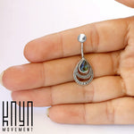 A hand holds the IBOSA Teardrop Belly Piercing Ring in Silver & Abalone Shell, a piece of jewelry from Kaya Movement. The charm on the 14 gauge navel belly ring features an inner layer reminiscent of abalone shell colors and outer layers with bead detailing, made from 316L surgical steel. The branding "Kaya Movement" appears in black text in the bottom left corner.
