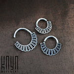 A photo displaying three Kaya Movement AZTEC Septum Rings in Silver, arranged in a triangular formation on a dark textured background. The 16 gauge, 925 silver body jewelry features crescent shapes with parallel lines extending outward from the inner edge, embodying a tribal boho design.