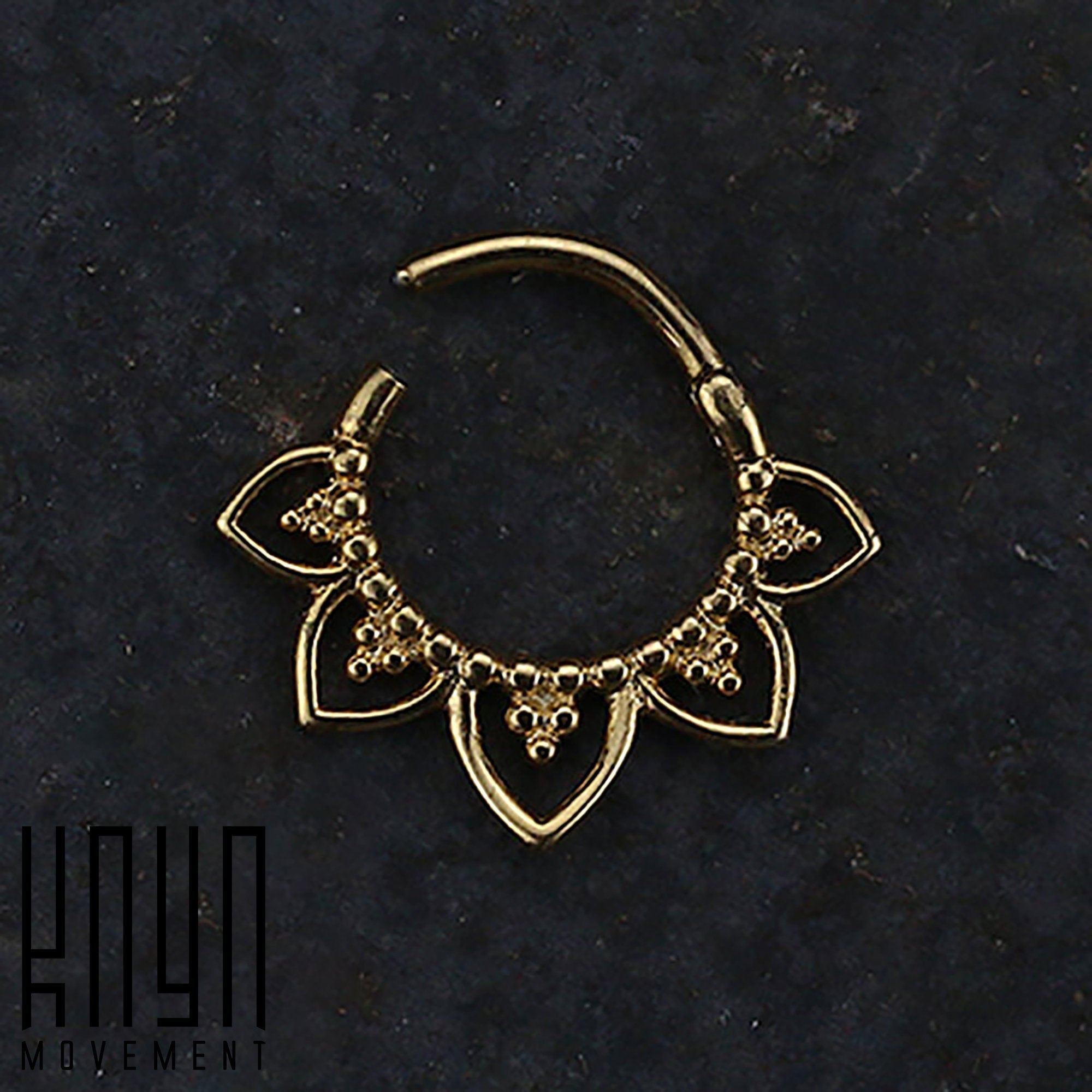 The MAWAR Lotus Flower Clicker Septum Ring in Gold, meticulously crafted from 316L Surgical Steel, is displayed against a dark background. The ring boasts an exquisite design with five petal-like extensions, each embellished with delicate bead accents. In the bottom left corner, the Kaya Movement logo is prominently featured.
