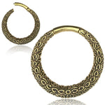 A close-up image displays a pair of PAWA Tribal Thick Hoop Ear Weights in Gold with Clicker by Kaya Movement. The earrings feature a detailed, raised floral pattern along their curved surface, giving them an ornate and vintage appearance reminiscent of classic brass jewelry. The background is plain white.