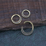 Three small MOON Seamless Rings in gold, made by Kaya Movement, with a hammered texture design lay on a wooden and leather surface. Two rings are closed, one is open, showcasing detailed metalwork. These minimalist gold brass body jewelry rings have a simple yet elegant look with an antique aesthetic.