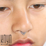 Close-up of a person's lower face showing a Triangle Sterling Silver Nose Septum Ring with V-shaped jewelry adorned with small gems. To the left, there is a logo with the text "Kaya Movement" in black. The person's skin is smooth and lips are slightly parted.