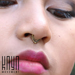 A close-up of a person's nose and lips showcases a decorative septum piercing featuring the LILY Seamless Teardrop Septum Ring in Gold, an 18-gauge piece adorned with tiny gold-like beads arranged in a V-shape. They are wearing pink lipstick, and the text "Kaya Movement" is visible in the bottom left corner.