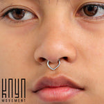 A close-up shot of a person's face, showcasing the TIKA Teardrop Clicker Ring in 316 Surgical Steel (16 gauge). The background is plain and minimalistic, emphasizing its minimalist design. The "Kaya Movement" logo is displayed in the bottom left corner.