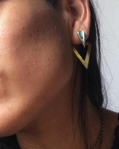 Close-up of a woman's ear wearing Kaya Movement's DIA Minimalist Triangle Ear Hangers in Gold & Abalone Shell. This sleek, geometric piece of body jewelry, featuring a gold-colored triangular hoop with a smaller abalone shell triangular stud above it, is perfect for anyone looking to make an elegant statement.