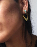 Close-up of a woman's ear wearing Kaya Movement's DIA Minimalist Triangle Ear Hangers in Gold & Abalone Shell. This sleek, geometric piece of body jewelry, featuring a gold-colored triangular hoop with a smaller abalone shell triangular stud above it, is perfect for anyone looking to make an elegant statement.