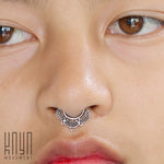 Close-up of a person's face focusing on a decorative septum piercing. The silver body jewelry is an elegant, 18g Silver Lotus Flower 8mm Septum Ring - Mandala Nose Ring with intricate design details from Kaya Movement. The image also shows part of the person's nose, eyes, and slightly parted lips. The word "KNYN" is in the bottom-left corner.
