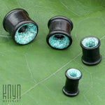 A photograph of four TOAN Round Saddle Tunnels in Wood & Turquoise, made by Kaya Movement, neatly arranged on a green leaf. Crafted from Ironwood and featuring turquoise stone inlays, the sizes vary with two larger ones at the top and two smaller ones at the bottom. The "Kaya Movement" logo is visible in the bottom left corner.