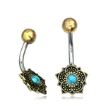 Two curved BLUE LOTUS Flower Belly Piercing Rings by Kaya Movement are featured. Each 14 ga ring, crafted from surgical steel jewelry, has a gold ball at the top and a detailed flower design at the bottom with a natural turquoise stone in the center. The intricate patterns of the flower design boast an antique gold finish.
