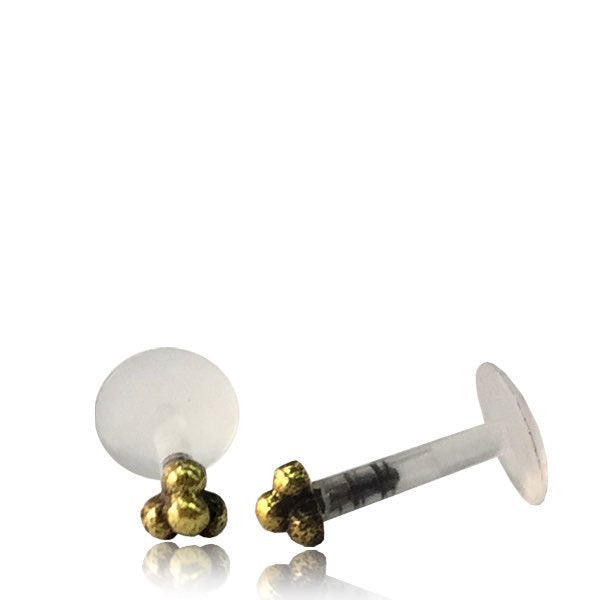 A pair of 16-gauge TRINITY Beaded Labret Studs in Gold by Kaya Movement, featuring clear bio-plastic push backings. One stud is positioned upright while the other lies on its side, both displayed on a reflective surface against a plain white background.