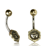 The Om Chakra Belly Piercing Rings in Gold by Kaya Movement, crafted from surgical steel with a 14 gauge curved bar and ornate hexagonal ends engraved with an Om symbol. Each belly button ring features a simple gold ball at the top, making them exquisite pieces of belly jewelry that are perfect for gift packaging.