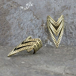 Presenting the IRA Chevron Ear Cuff in Gold from Kaya Movement, this exquisite accessory features a V-shaped design adorned with intricate tribal patterns. Displayed against a textured gray stone background, one ear cuff stands upright while the other lies on its side, effectively showcasing different angles of its adjustable size.