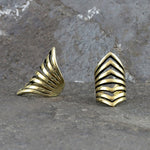 The LORA Chevron Cage Ear Cuff in Gold by Kaya Movement is displayed against a textured stone background. Each cuff showcases an intricate design of multiple layered, chevron-shaped bands, creating a unique and bold aesthetic. The cuffs appear to be handmade and have a polished finish, reminiscent of elegant craftsmanship.