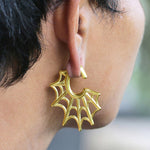 Close-up image of a person's ear wearing Kaya Movement's Spider Web Gothic Steel Ear Hangers in Gold (2 gauge). The intricate tribal design features broad, web-like patterns extending outward, adding an artistic and stylish touch.