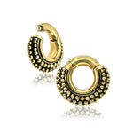 Close-up of a pair of MAHAL Small Hoop Ear Weights in Gold with Clicker from Kaya Movement. Featuring a raised dotted pattern on the outer edge for a textured and ornate appearance, these 2-gauge earrings have an antique look. The inner part of the hoops is smooth, contrasting with the detailed exterior.