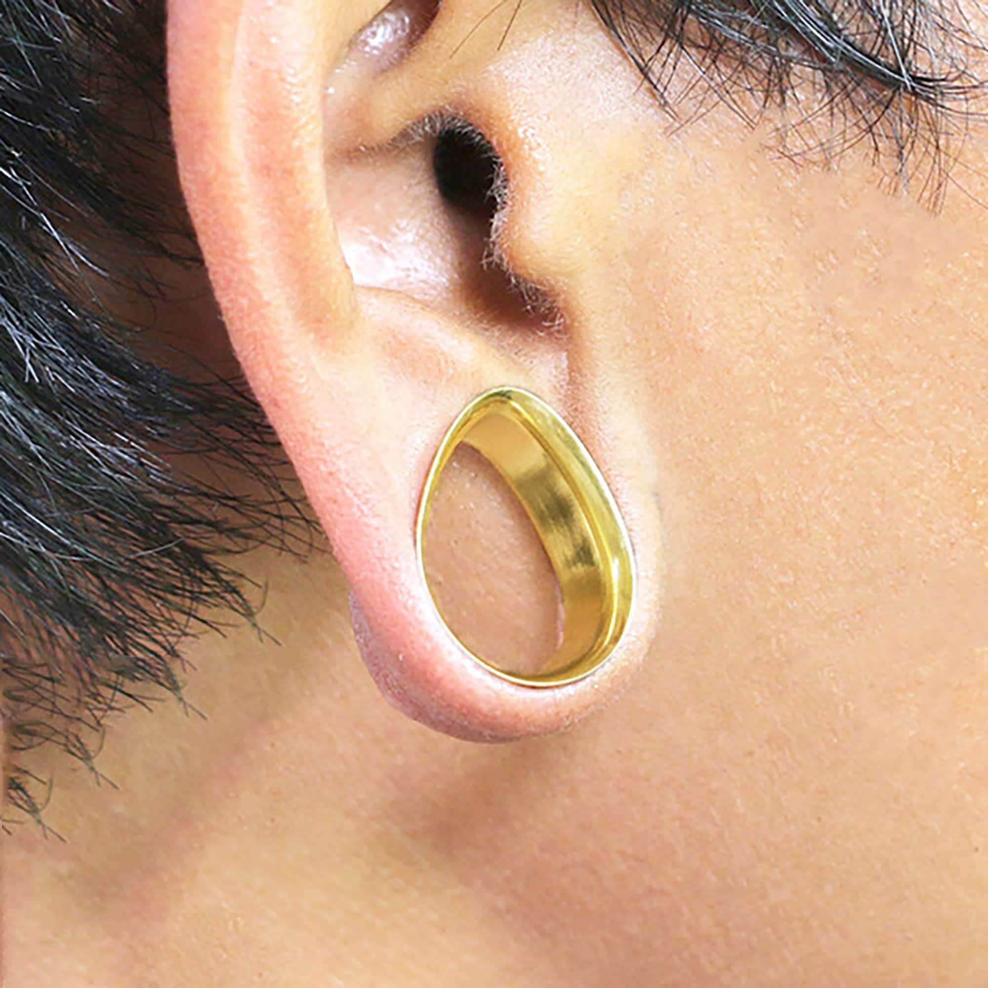 A close-up of an ear with a teardrop-shaped Kaya Movement surgical steel ear tunnel inserted through the earlobe, showcasing a stretched ear piercing. The Teardrop Tunnel has smooth and polished edges, adding a touch of elegance to the stretched lobe.