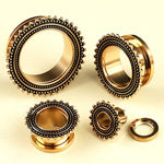 Four rose gold plugs from Kaya Movement, crafted from stainless steel and designed as Flesh Tunnel piercings, are arranged on a light surface. These ear gauges for small gauged ears feature intricate ornamental detailing with small black bead-like patterns on their outer edges, resembling the artistry of a tribal plug.