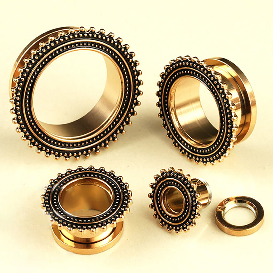 Four rose gold plugs from Kaya Movement, crafted from stainless steel and designed as Flesh Tunnel piercings, are arranged on a light surface. These ear gauges for small gauged ears feature intricate ornamental detailing with small black bead-like patterns on their outer edges, resembling the artistry of a tribal plug.