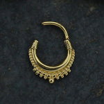 A single gold earring from the Kaya Movement collection, specifically the Hinged Teardrop Tribal Septum Ring Clicker (16g) designed for conch, daith, helix body piercing or as a cartilage earring, is displayed on a dark textured background. Its intricate detailing and small beads along the bottom edge evoke tribal jewelry. The earring is open, revealing its craftsmanship akin to that of a finely crafted gold septum ring.