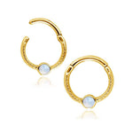 A pair of Gold Opal Hinged Septum Nose Ring Clickers crafted by Kaya Movement, measuring 8mm and designed for a 16g piercing, features a delicate patterned texture. Each clicker showcases a single round white opal set into the middle of the hoop, adding an elegant touch to the design. These versatile pieces can also be worn as Rook, Daith, or Helix Piercing Jewelry.