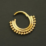 A single Gold Septum Clicker from Kaya Movement lies on a flat, dark surface. The 16g, 8mm hinged septum ring features a semi-circle design adorned with small, evenly spaced gold beads along its outer edge, giving it a decorative and ornate appearance.
