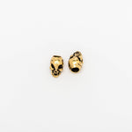 Two small gold-colored charms, perfect as Viking Hair Beads Accessories by Kaya Movement, are placed on a plain white background. These Alien Vampire Carved Skull Dreadlocks Beads Jewellery feature hollowed eyes and nose cavities with detailed facial features. One charm is shown from the front, while the other is displayed at an angle. Ideal for use as dreadlock accessories or unique brass hair beads, these beard accessories add a distinctive touch to your style.