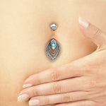 Close-up of a person's hand placed near a decorative navel piercing jewelry. The Kaya Movement Belly Button Teardrop Piercing Jewelry With Abalone features a circular stud above two intricate tear-drop shaped designs, with the inner tear-drop adorned with an iridescent blue abalone gem. Crafted from Sterling Silver 925, this Belly Bar 14g showcases an organic marquise design using real seashells.