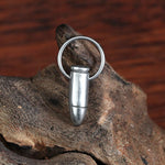 A pair of Silver Bullet Gun Dangle Earrings from Kaya Movement, complete with delicate charms and hypoallergenic hoops, resting on a textured wooden surface. The wood has a natural, rugged appearance with various shades of brown.