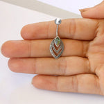 A hand holds a Kaya Movement Sterling Silver 925 Belly Button Teardrop Piercing Jewelry with a decorative double-layered design. The outer layer features intricate engravings, while the inner teardrop has a small, reflective green abalone stone at the center. The background is plain white.