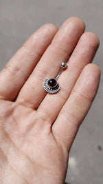A hand holding a piece of Kaya Movement's sterling silver belly button jewelry, featuring a mother of pearl nacre gemstone at its center. The navel piercing showcases a semi-circle design with small, evenly spaced extensions along the curved edge. The jewelry is delicate and small, resting gently on the palm, likely intended as eye-catching belly button jewelry.